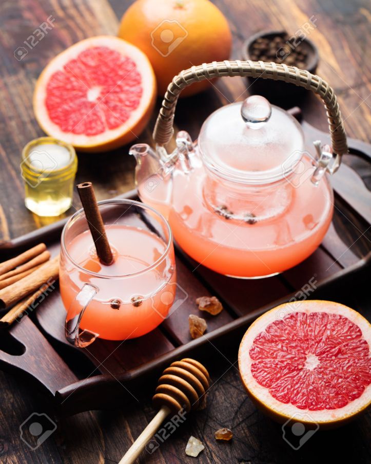 Grapefruit herbal tea with spices and honey in a glass teapot and cup on a dark wooden background